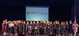 A jubilant group of CBD College graduates celebrating their academic achievement, with the college's logo displayed proudly in the background.