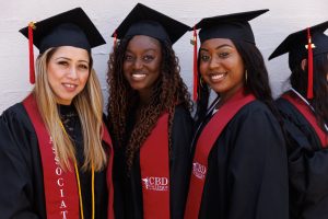 Three female graduates from CBD College celebrating their graduation ceremony, smiling and posing for a photo.