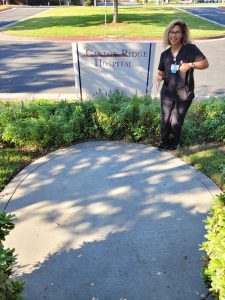 Corinne Ramaker, a graduate of the Occupational Therapy Assistant program at CBD College, stands proudly in front of the Canyon Ridge Hospital monument, appearing smaile in the image.
