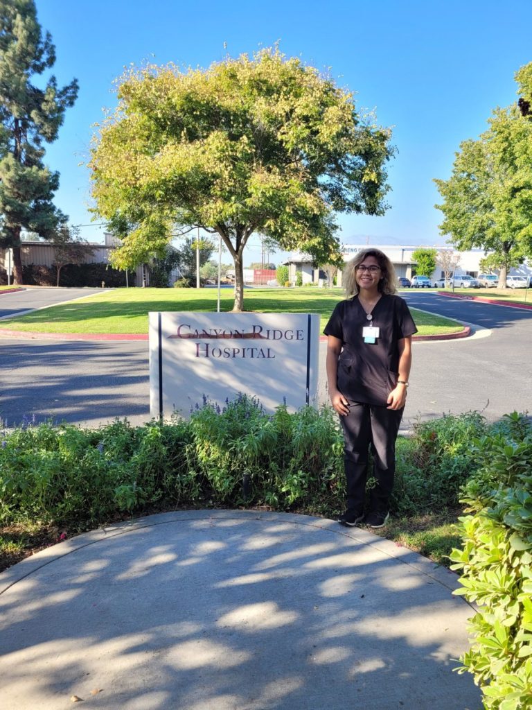 Corinne Ramaker, a graduate of the Occupational Therapy Assistant program at CBD College, stands proudly in front of the Canyon Ridge Hospital monument, appearing smaile in the image.