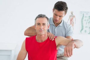 A male physical therapist stretches a mature man's arm at the hospital.